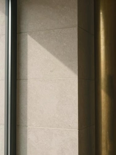 Tight abstract crop of a modern limestone architectural column, soft natural window light, warm shadows, 35mm