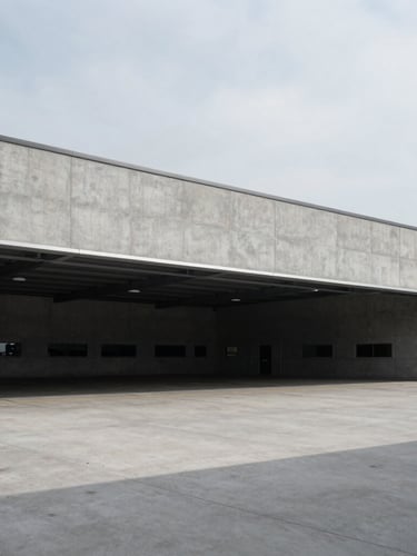 Wide architectural shot of a modern concrete logistics terminal, sharp shadows, cool overcast daylight, minimalist composition