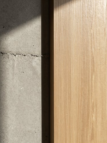 Close-up of premium materials, raw concrete meets a warm sand-colored oak panel, soft natural side-light, architectural details, elegant shadows