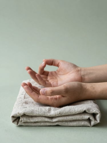 Medium close-up, slightly off-center — two hands resting in a mudra position on a folded linen cloth, soft diffused daylight from above, muted sage-green background, peaceful and unhurried still-life quality