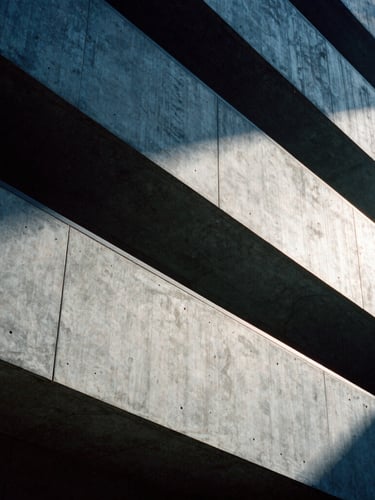 Architectural crop of a modern concrete building facade, sharp diagonal shadows, high-contrast side-lighting, 35mm film