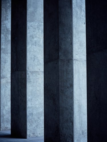 Architectural concrete lines with dramatic side-lighting, cool blue and deep charcoal tones, high-contrast shadows, 35mm lens.