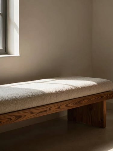 A sunlit window bench in a minimalist plaster room, low-angle morning light casting deep shadows on rich oak grain and textured bouclé fabric, 50mm lens.