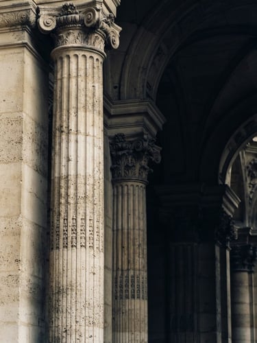 Macro detail of classic stone architectural columns and deep shadows, soft overcast daylight, muted navy and warm champagne tones, 35mm.