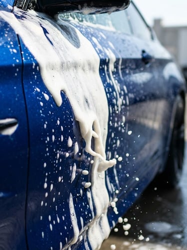 Crisp commercial photography of thick, vibrant white active foam sliding down a deep blue metallic car panel, high-speed shutter capturing water droplets, bright natural daylight, 50mm