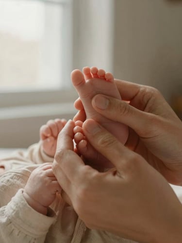 A close-up of a mother's hands gently holding a newborn baby's feet, soft linen textures, warm morning window light, shallow depth of field, warm editorial photography