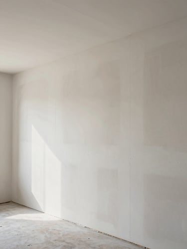 Wide architectural shot of freshly installed drywall panels in a commercial interior, seams aligned with precision, north-facing daylight raking across the surface revealing texture and uniformity, no workers visible, single vanishing-point perspective