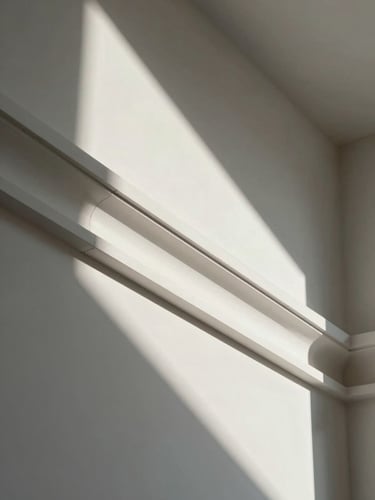 Close-up of a freshly installed gypsum sanca profile in an empty room, sharp shadow line along the molding edge, north-facing daylight raking across the white surface to reveal the precision of the joint, no people, no furniture, architectural detail photography