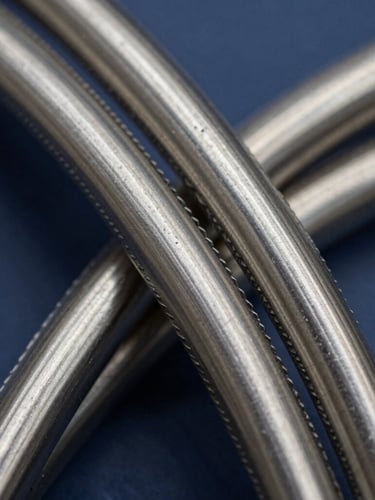 Macro shot of high-pressure steel-wire hose braids, showing metallic reflections, deep navy background, cool steel tones, 35mm photography