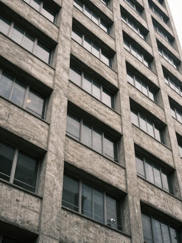 Close architectural detail of a Lagos mid-rise building facade — rendered concrete panels and aluminium window frames under even overcast daylight, shot from street level looking up at a slight angle to show structural quality and finish, no people