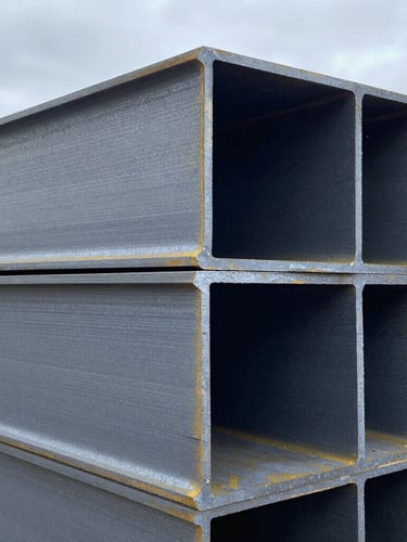 Close-up of massive stacked steel I-beams in a cold overcast warehouse, high contrast steel textures, sharp industrial details, 35mm lens