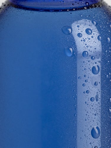 Macro close-up of pure water droplets streaming down a frosted deep blue bottle, sharp focus on condensation, high-contrast crisp studio lighting.