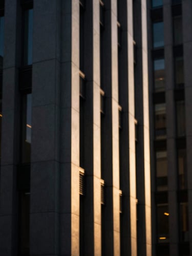 Dramatic architectural lines of a modern corporate headquarters in Madrid, sharp side-lighting, deep shadows with warm golden highlights, shallow depth of field, 35mm lens