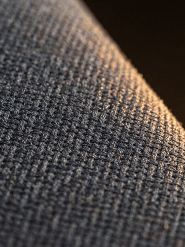Macro close-up of structured grey uniform twill fabric, highlighting the diagonal weave pattern, dramatic side lighting, dark moody background