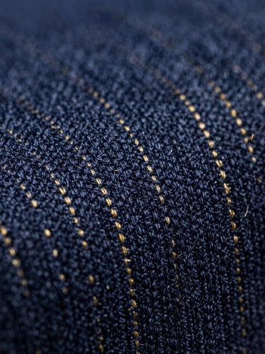 Extreme macro close-up of premium navy blue cotton fabric weave, showing detailed thread texture and gold fiber accents, dramatic studio side lighting, shallow depth of field