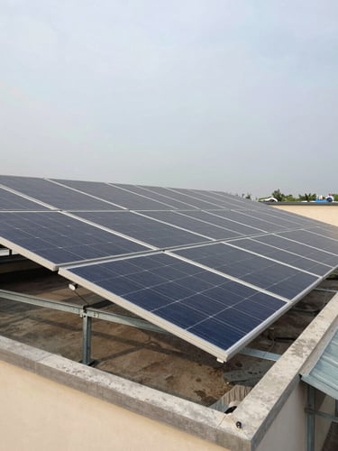 Wide environmental shot from ground level looking up at a completed residential rooftop solar installation in Bihar, full panel array visible against an overcast daylight sky, galvanized mounting structure clearly in frame, no people, natural muted light showing panel texture and roof footprint