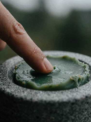 Extreme macro close-up of a warm fingertip scraping solid botanical wax from a hand-carved grey soapstone compact, moody overcast daylight, deep shadows.