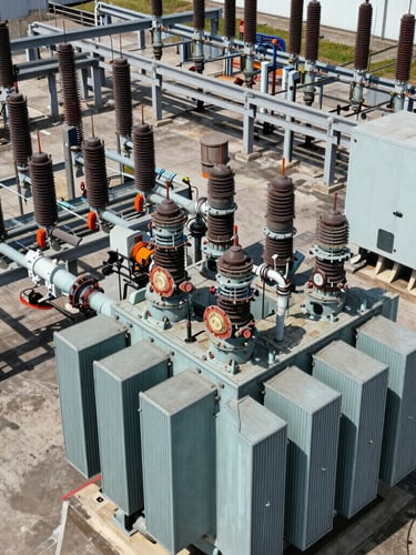 Close-up of heavy electrical switchgear and massive transformer conduits at an industrial substation, harsh direct sunlight, gritty technical detail