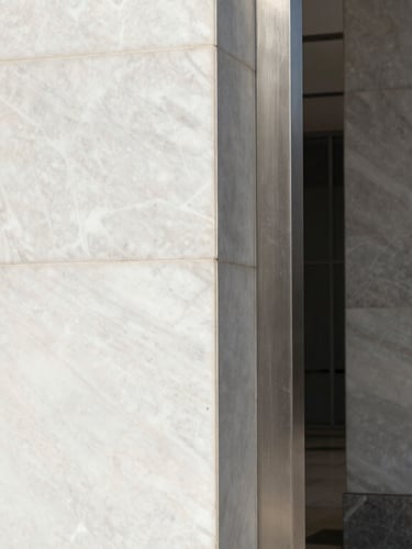 Macro detail of polished white marble and brushed steel architectural columns in a Riyadh corporate lobby, high-contrast daylight, sharp shadows.