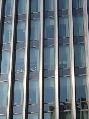 Close-up of structured glass and brushed steel facade of a modern corporate headquarters in Riyadh, sharp high-contrast daylight.