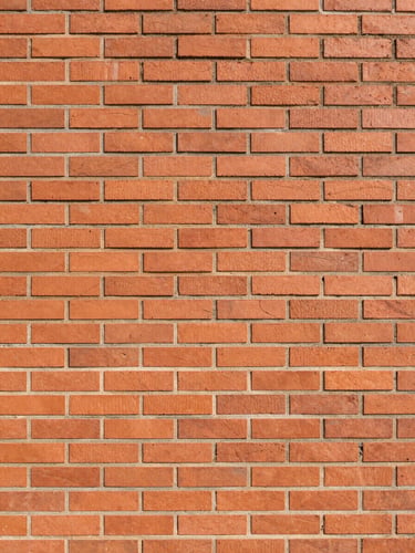 Straight eye-level architectural shot of raw Porotherm brickwork under bright morning sunlight, showing clean mortar lines and precise alignment, warm clay tones, architectural framing with negative space.