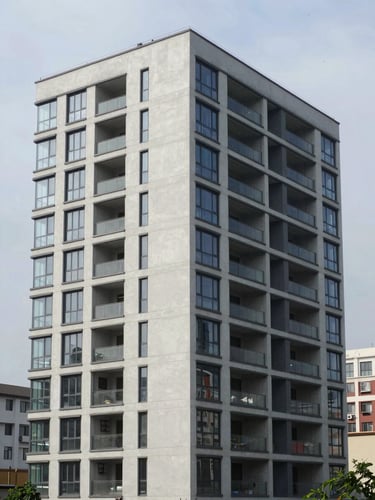 Eye-level wide shot of a completed multi-storey commercial building exterior, clean facade with concrete and glass panels, photographed in natural overcast daylight — no people, architectural clean-up framing, full building height visible, urban context at the edges
