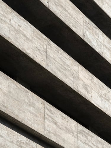 High-contrast architectural details of a brutalist concrete building, sharp diagonal shadows, dramatic natural side-lighting, clean lines, minimalist framing.