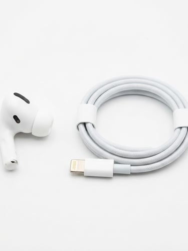 Bright, high-key studio shot of a modern wireless earbud and a charging cable arranged neatly on a white backdrop, sharp focus, clean shadows.