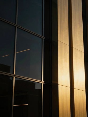 Cinematic close-up of high-end architectural materials, dark glass and brushed gold metal, dramatic low-key lighting with sharp golden-hour window reflections, 35mm