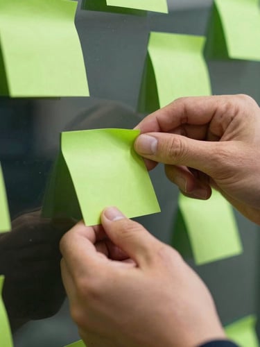 Close-up of hands placing a neon green sticky note on a glass partition, sharp focus, dramatic natural light.