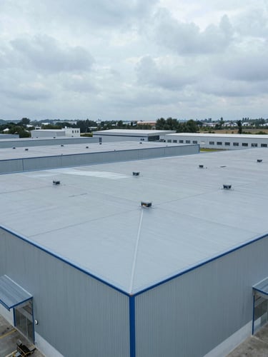 Wide-angle drone shot of a newly completed logistics warehouse roof, crisp overcast daylight, metallic blues and cool grays, 35mm.