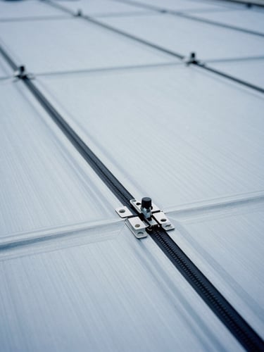 Close-up of a double-lock zip-roofing seam being profiled on-site by specialized machinery, metallic blue tone, crisp overcast light, 35mm