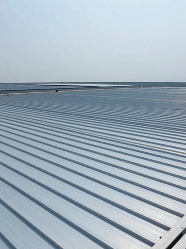 Wide-angle technical shot of a massive industrial roof installation, showing continuous zip-roofing profiles stretching across the structure under crisp overcast daylight, cool metallic blue tones, 35mm