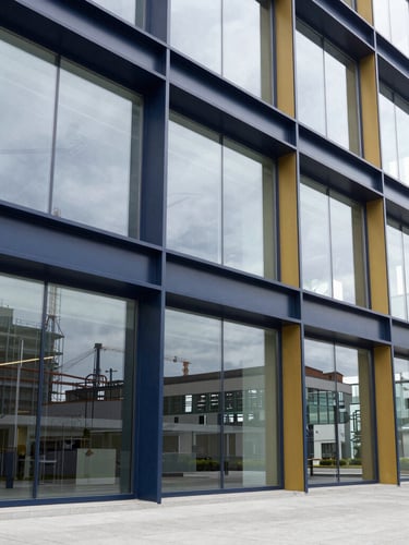 A bright corporate office with large glass windows showing industrial architecture in the background, sharp natural daylight, premium editorial style