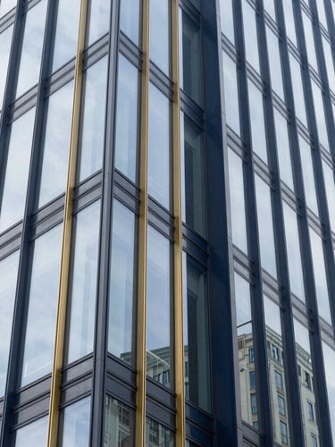 Vertical architectural shot of a modern glass office building facade, sharp geometric lines pointing upward, bright daylight, editorial style