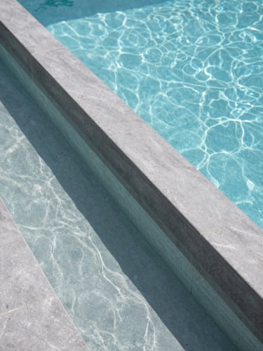 Close-up of a luxury zero-edge pool overflow channel with crystal clear water and precise graphite grey tiling under bright daylight