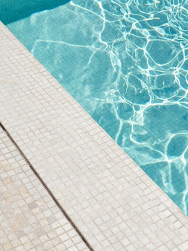 Macro architectural photograph of perfectly aligned Italian mosaic tiles under crystal clear water, sharp geometric pool edge, bright Mediterranean daylight