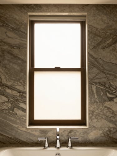 Straight-on architectural photography of a luxury master bathroom with bookmatched veined marble walls, warm natural window light, rich moody tones, 35mm lens.