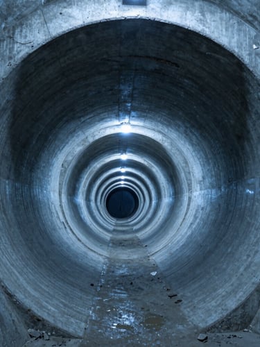 Wide-angle industrial documentary of deep alpine tunnel bore, massive concrete lining arches, cool blue subterranean light, high contrast.