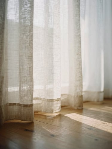 Sunlight filtering softly through a linen window curtain onto a clean wooden floor, quiet and calming atmosphere, muted earth tones