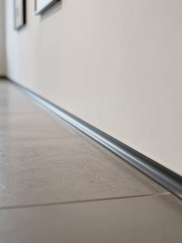 Macro close-up of a seamless, high-gloss vinyl floor wrap edge being perfectly aligned to a gallery wall, bright clean venue daylight