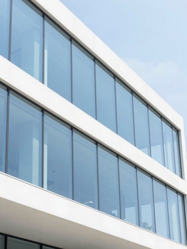 Bright architectural photography, high-key natural daylight, clean white and electric blue tones, sharp focus, 35mm lens showing a modern minimalist office with glass walls and clean structural lines.
