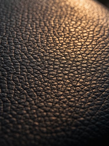 Extreme close-up side-lit dark desaturated leather grain, dramatic chiaroscuro lighting, warm golden-hour undertones, showcasing micro-precision texture and grade-A selection.