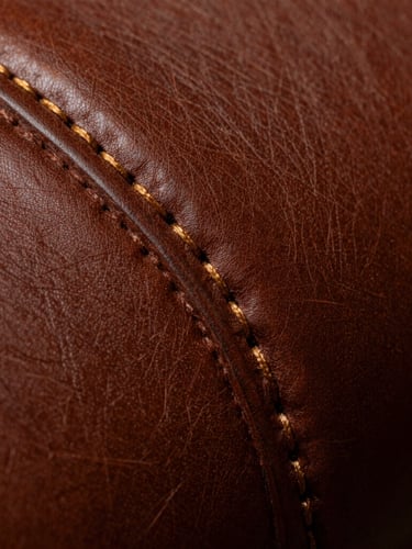 Extreme macro close-up of precise double-stitching on rich desaturated brown leather, dramatic side lighting, chiaroscuro, showing fine grain texture and gold thread.