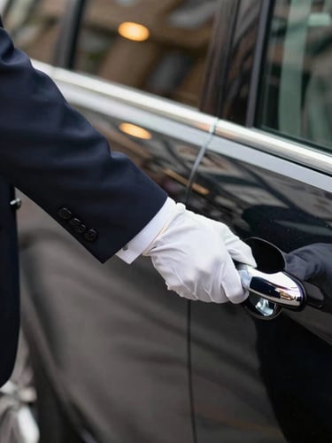 Close-up of a professional chauffeur in a dark tailored suit and white gloves opening the door of a black Mercedes-Benz V-Klasse, soft ambient streetlights reflecting on the polished chrome handle