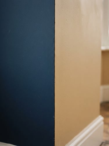 Vue macro d'un coin de mur fraîchement peint avec une ligne de démarcation parfaite, lumière naturelle côtière douce, tons bleu marine et sable, 35mm lens, architectural detail.