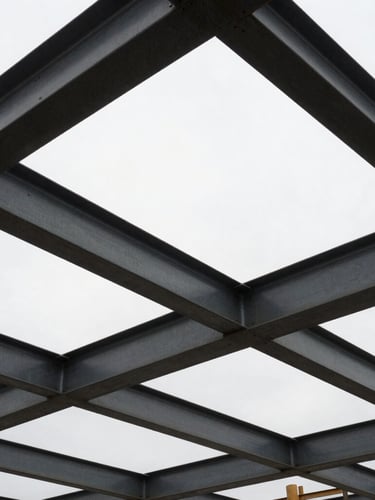 Low-angle heroic shot of an active construction site in Belleville, steel beams framing an overcast sky, high-contrast industrial shadows, 35mm lens.