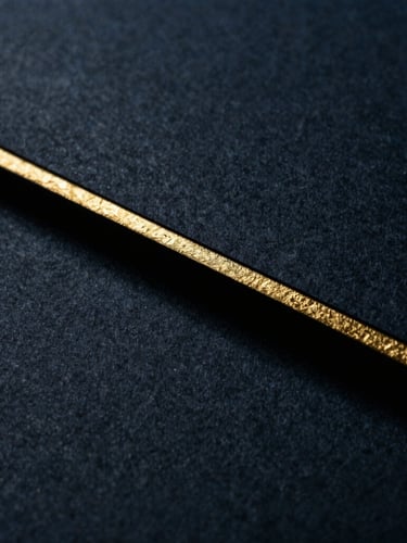 Macro photograph of heavy textured paper with gold leaf edge, casting a deep shadow, moody low-key lighting, dark navy tones.