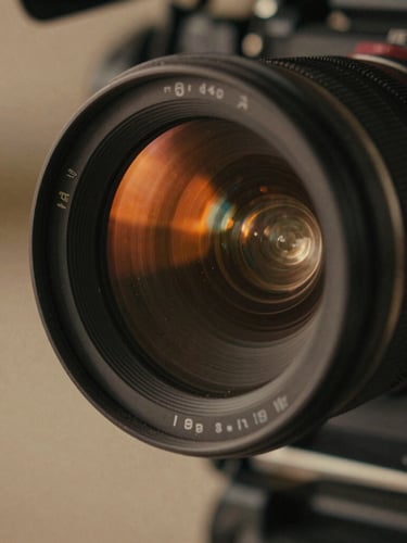 Close-up of a high-end cinema camera lens, dust particles catching a dramatic warm orange light flare, shallow depth of field, cinematic film photography, deep shadows.