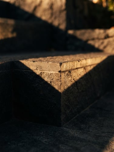 Macro photograph of modern architectural stone steps with sharp geometric shadows, warm golden sunlight brushing the edges, premium editorial, 35mm